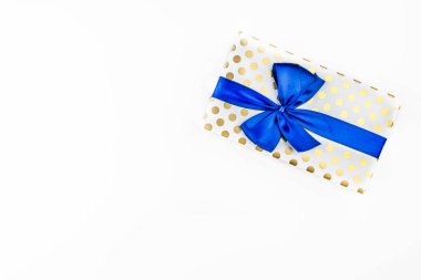 A gift wrapped in white paper with gold circles wrapped in a blue ribbon tied in a bow, isolated on a white background, top view.