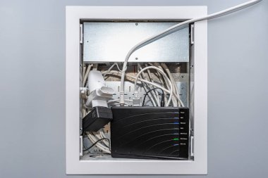 Garajın gri duvarındaki bir kutuya yerleştirilmiş, içinde internet modemi ve anten kabloları olan açık bir multimedya kutusu..