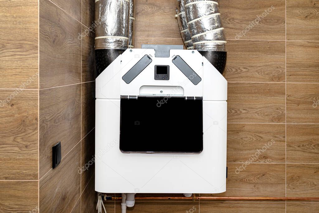 Home mechanical ventilation with heat recovery hanging on the wall in a modern gas boiler room with brown ceramic tiles imitating wood.