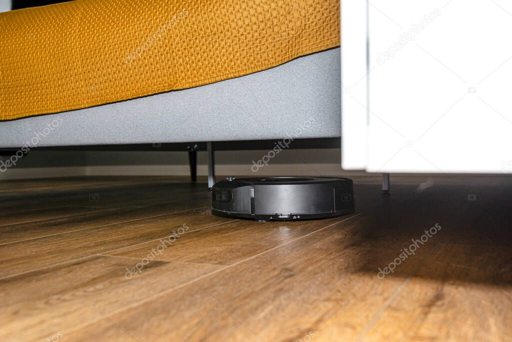 A modern robotic vacuum cleaner cleans vinyl panels under bedroom furniture, an autonomous cleaning robot.