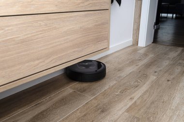 Modern bir robot süpürgesi banyodaki seramik fayansları temizler. Duvara monte edilmiş dolap, otonom bir temizlik robotu..