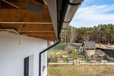 Arka planda seramik kiremitlerle kaplı bir çatıdaki metal, siyah oluk. Bir orman, alt manzara..