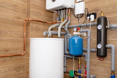 Seramik kiremitlerle kaplı bir kazan dairesindeki modern bir gaz kazanı için su tankı ve gaz boruları..