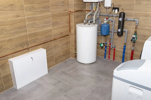 A modern gas boiler for natural gas, installed in a boiler room lined with ceramic tiles, visible 120 liter hot water tank and underfloor heating manifold.