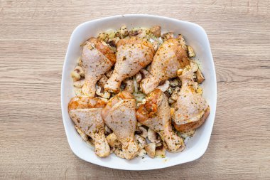 Mantarlı bir tabağa yağ ve baharat sürülmüş çiğ tavuk budu. Pişirmeye hazır..