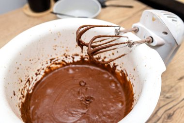 Bir çırpma kabı yanında duran el çırpma makinesi, hamur hamur kalın sıvı kahverengi haldedir..