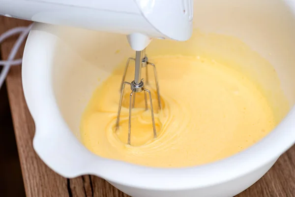 Kneading the dough using a hand mixer with a whisk, the dough is in a yellow liquid state.