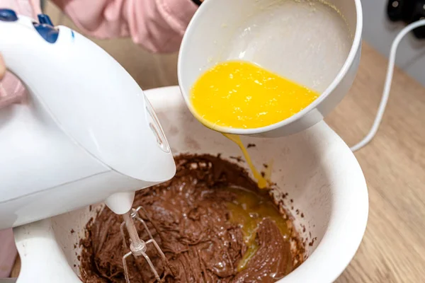 Mixing the dough with a hand mixer with a whisk with melted butter added, the dough is in a thick liquid brown mass.