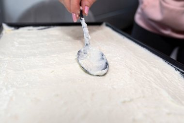 Kadın fırında kakaolu kekin üzerine krema ve krema koymak için kaşık kullanıyor..