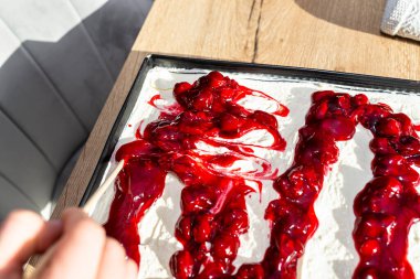 Bir kadın hazır Japon pastasını süzme peynir, krem şanti ve vişne sosuyla süslemek için çubuk kullanır..