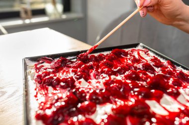 Bir kadın hazır Japon pastasını süzme peynir, krem şanti ve vişne sosuyla süslemek için çubuk kullanır..