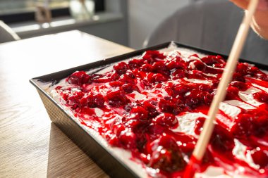 Bir kadın hazır Japon pastasını süzme peynir, krem şanti ve vişne sosuyla süslemek için çubuk kullanır..
