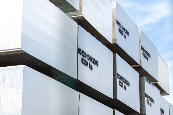 Heavy aluminum bars stacked on top of each other in an aluminum smelting plant, against the blue sky.