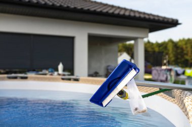 Cleaning the home pool in the garden with a brush, cleaning and maintenance of the home pool. clipart