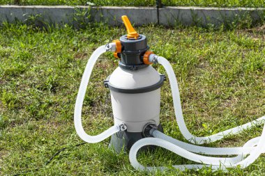 Bahçe havuzu temizliği için büyük kum pompası, şeffaf su hortumları görünür..