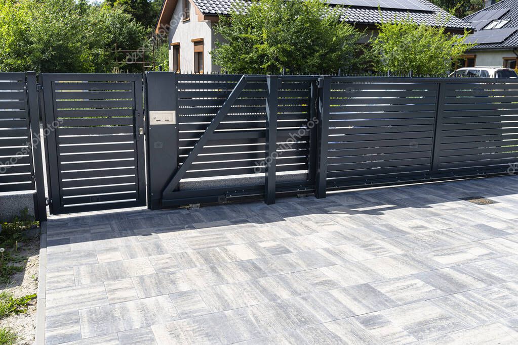 A modern panel fence in anthracite color, a visible sliding gate to the garage and a wicket with a letterbox.