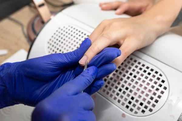 The manicurist cuts the nail cuticles with small scissors, wearing blue latex gloves.