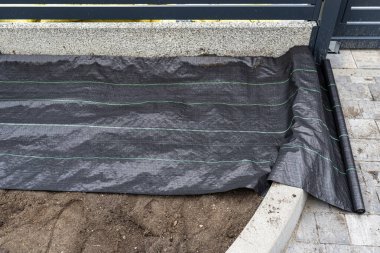 The plowed garden in front of the fence in the house, covered with black agrofiber, modern panel fencing visible
