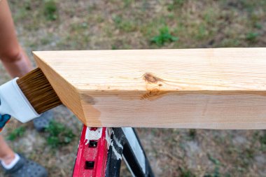 The woman impregnates raw planed wooden pine beams with dimensions of 100x100mm with a colorless impregnation.