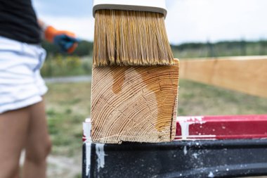 The woman impregnates raw planed wooden pine beams with dimensions of 100x100mm with a colorless impregnation.