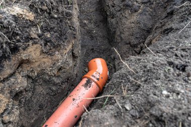 An orange plastic pipe from a septic tank with a diameter of 160 mm lying in a ditch.