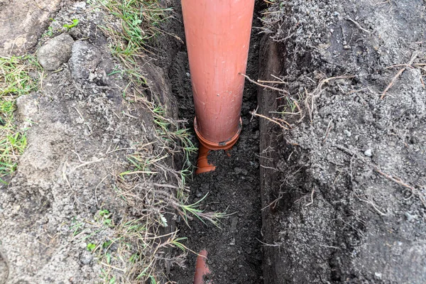 An orange plastic pipe from a septic tank with a diameter of 160 mm lying in a ditch, visible pipe for revision.