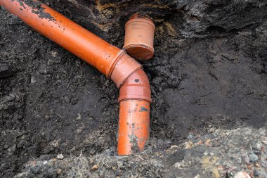 An orange plastic pipe from a septic tank with a diameter of 160 mm lying in a ditch, blind pipe visible.