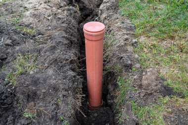 An orange plastic pipe from a septic tank with a diameter of 160 mm lying in a ditch, visible pipe for revision.