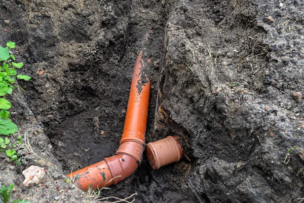 An orange plastic pipe from a septic tank with a diameter of 160 mm lying in a ditch, blind pipe visible.