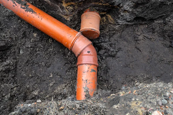 An orange plastic pipe from a septic tank with a diameter of 160 mm lying in a ditch, blind pipe visible.