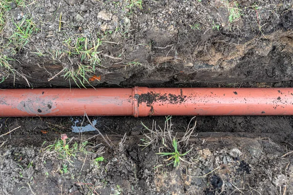 An orange plastic pipe from a septic tank with a diameter of 160 mm lying in a ditch.