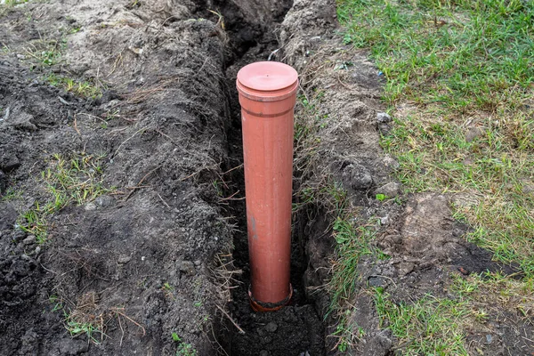 An orange plastic pipe from a septic tank with a diameter of 160 mm lying in a ditch, visible pipe for revision.