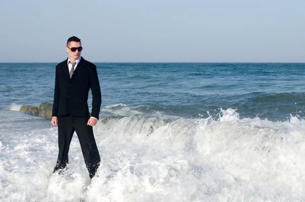 Joven hombre de negocios hermoso disfrutando de su tiempo en una playa mientras las olas están golpeando la orilla — Foto de Stock