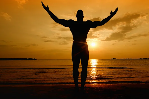 Silhouette eines Bodybuilders, der beim Sonnenaufgang am Strand posiert — Stockfoto