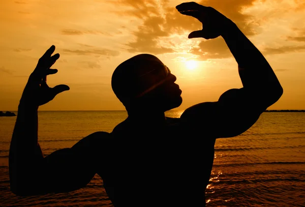 Silhuett av kroppsbyggare poserar på soluppgången på stranden — Stockfoto