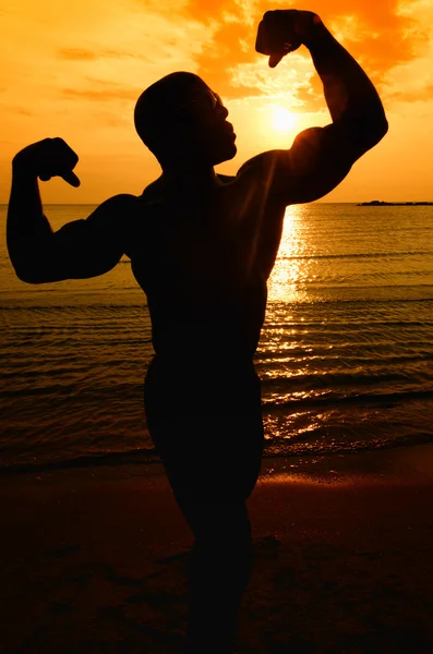 Silhouette di bodybuilder in posa all'alba sulla spiaggia — Foto Stock