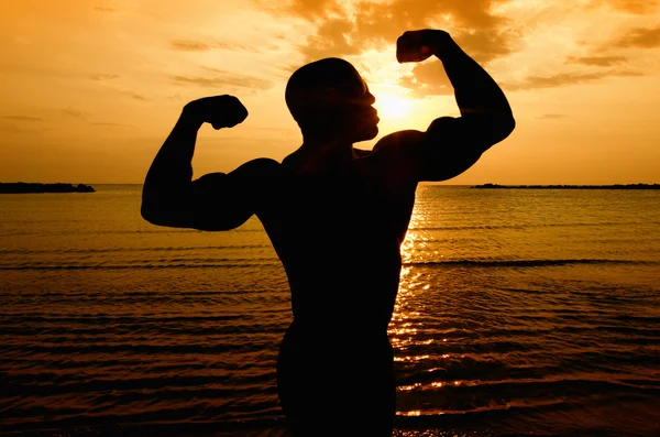 Σιλουέτα του bodybuilder που παρουσιάζουν κατά την Ανατολή του ηλίου στην παραλία — Φωτογραφία Αρχείου