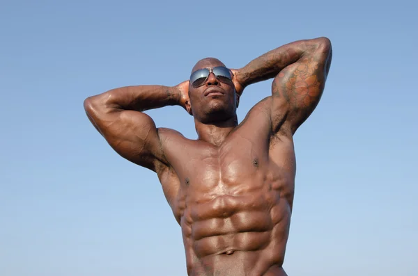 Hombre fuerte culturista con abdominales perfectos, hombros, bíceps, tríceps y pecho posando con el cielo como fondo —  Fotos de Stock