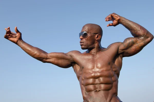 Hombre fuerte culturista con abdominales perfectos, hombros, bíceps, tríceps y pecho posando con el cielo como fondo —  Fotos de Stock
