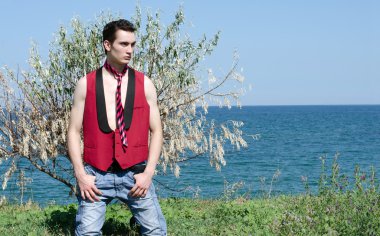 genç adam kırmızı kravat, ceket ve kot pantolon giyiyor sahilde rahatlatıcı