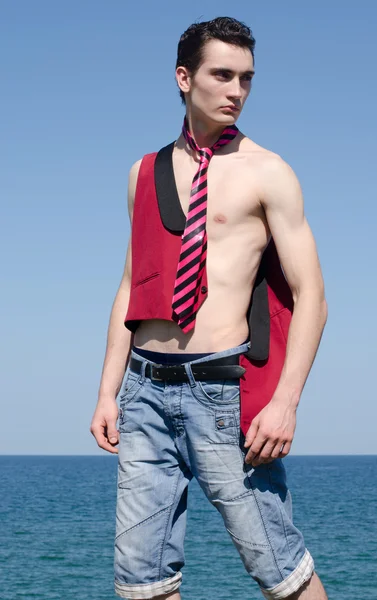 Jonge man ontspannen op het strand dragen een rode stropdas, jas en jeans — Stockfoto