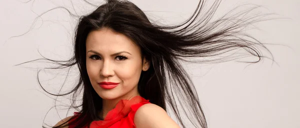 Beautiful brunette girl with long hair. Young attractive woman with red lips wearing a red blouse with hair in the air — Stock Photo, Image