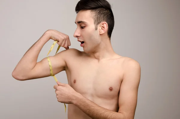 Hombre flaco midiendo sus pequeños bíceps con un centímetro —  Fotos de Stock