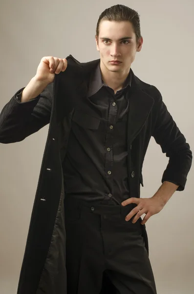 Jeune homme d'affaires vêtu d'une chemise noire, pantalon et portant un long manteau — Photo