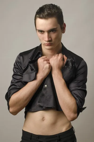 Sexy beautiful young man wearing a black shirt and undressing — Stock Photo, Image