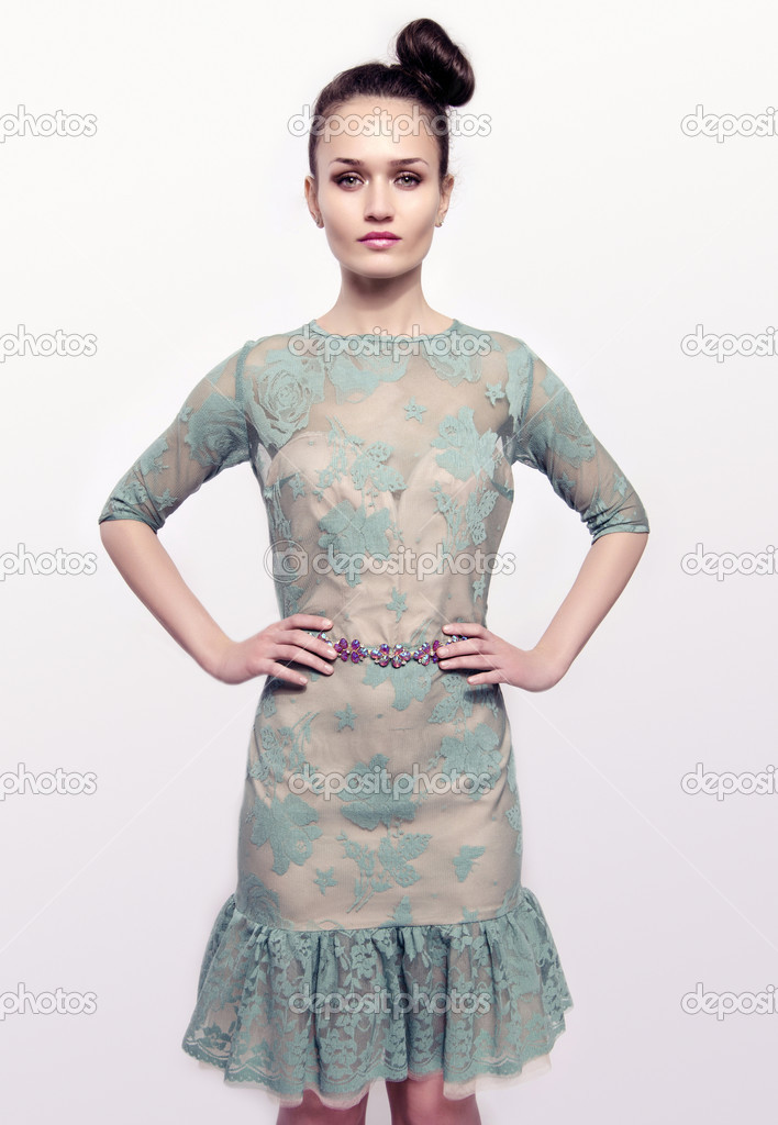 Beautiful brunette woman wearing a green lace dress and holding her hand on her waist. Girl posing fashion