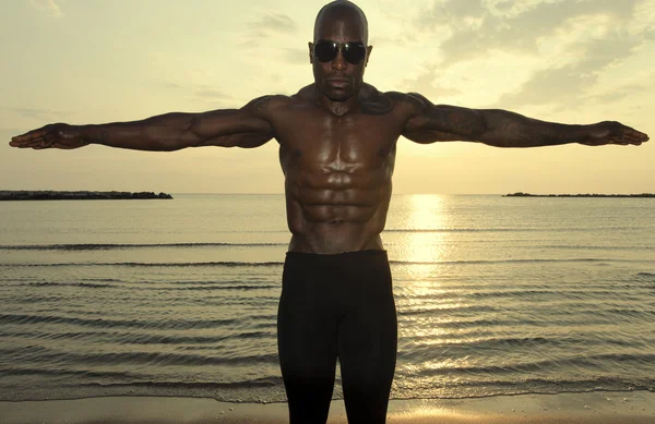 Bodybuilder noir seins nus. Homme fort avec abdos, épaules, biceps, triceps et poitrine parfaits posant au lever du soleil — Photo