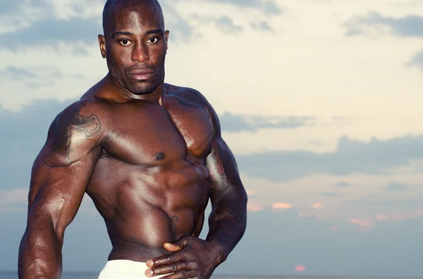 Svart bodybuilder topless. stark man med perfekta abs, axlar, biceps, triceps och bröst poserar på sunrise — Stockfoto