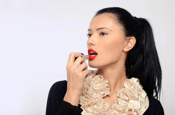 Portret van een mooie brunette vrouw het toepassen van rode lippenstift op haar lippen. — Stockfoto