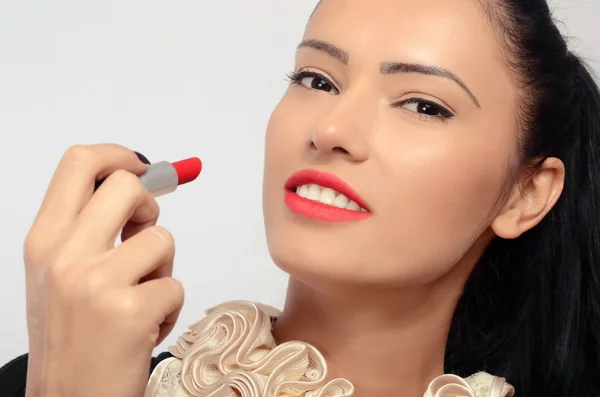 Portrait of a beautiful brunette woman applying red lipstick on her lips. Woman holding with her hand with black fingernails a red lipstick — Stock Photo, Image